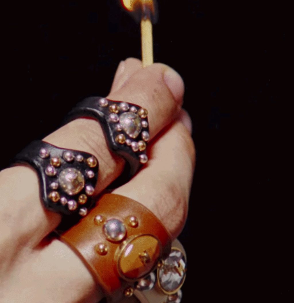 Hand in studded leather rings lighting a match against black